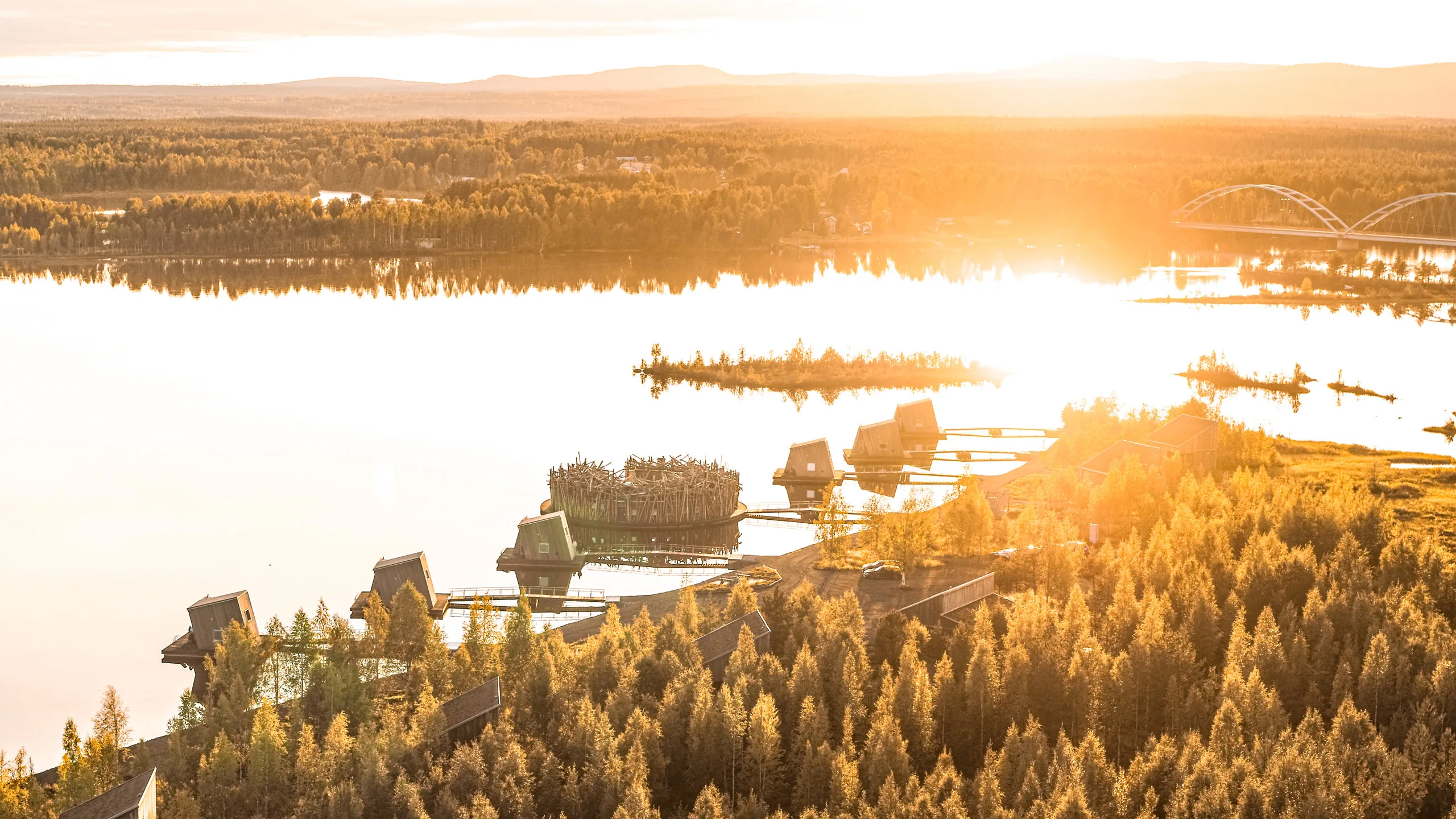 Aerial panoramic view of Arctic Bath floating spa, cabins and the Lule River at golden sunset