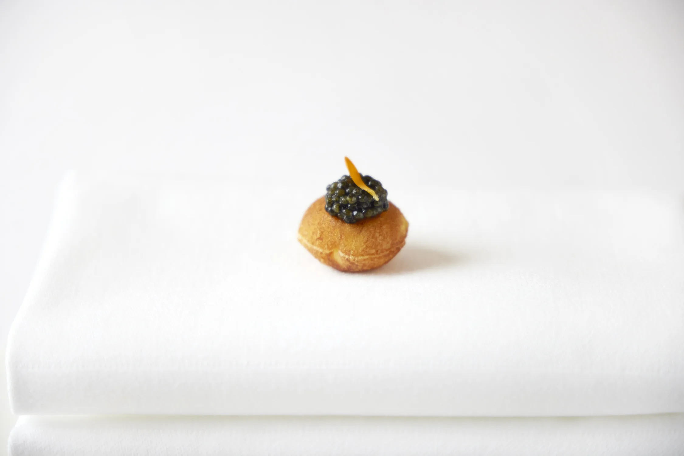 Small golden blini topped with caviar and orange zest on a white napkin