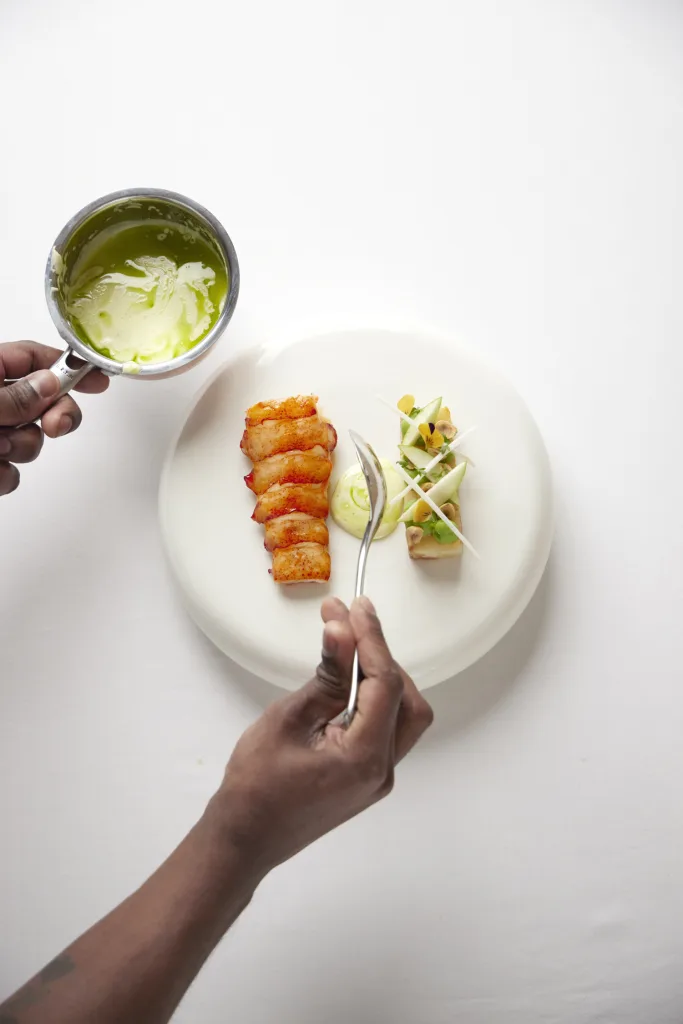 Chef plating lobster with green herb sauce on a white plate, overhead view
