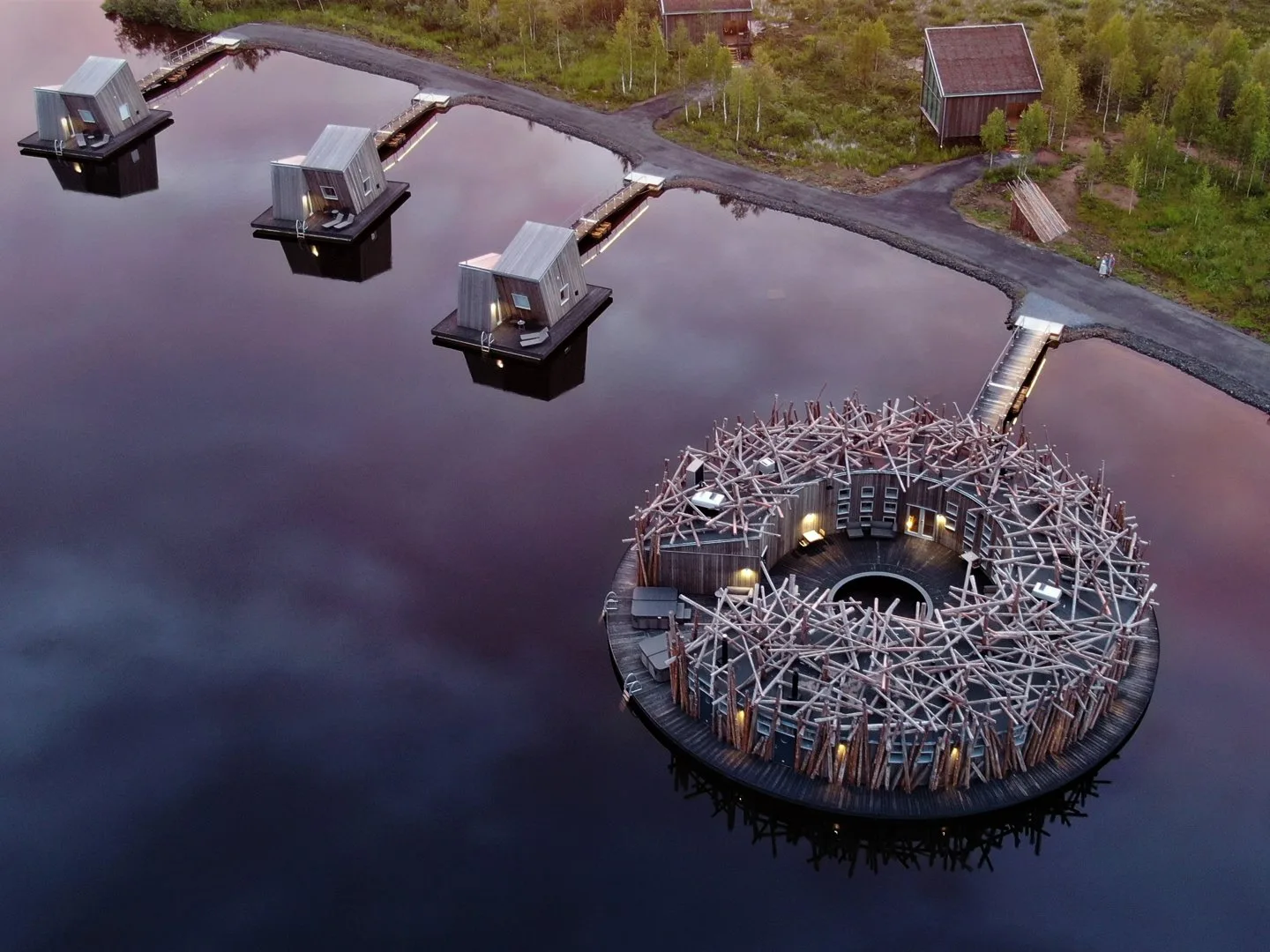 Aerial dusk view of Arctic Bath with glowing cabins reflecting in purple twilight water on the Lule River