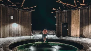 Man descending into the illuminated cold plunge at Arctic Bath's snowy circular courtyard at night