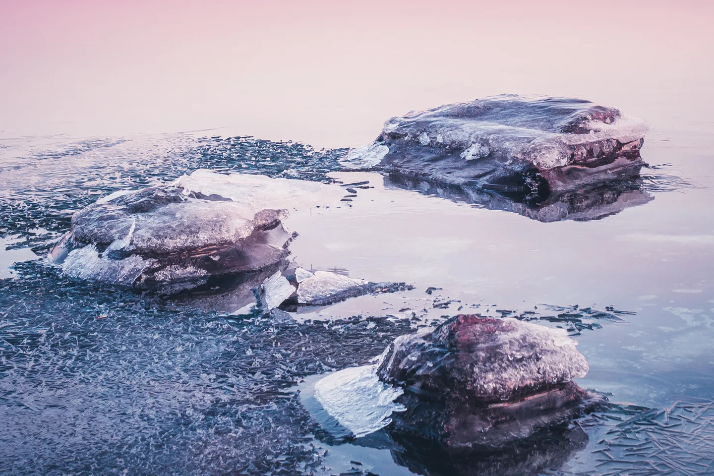 Ice-covered rocks protruding from partially frozen river water in pastel pink twilight light
