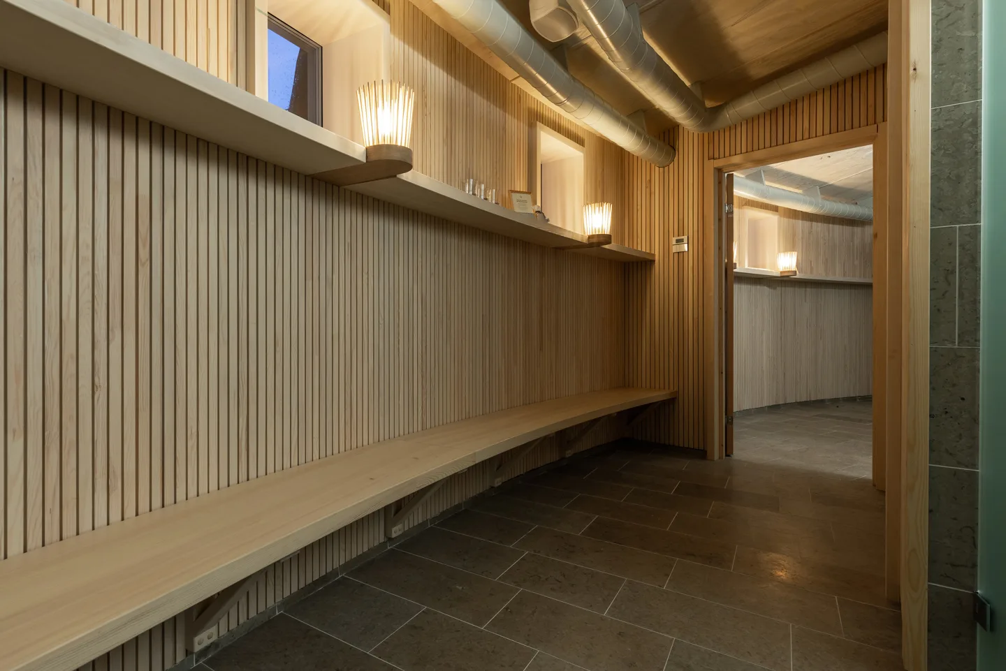 Wood-slatted spa changing area with bench, coat hooks and warm stick-style wall lamps