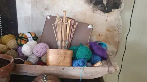 Hand-carved wooden trough holding colorful yarn balls, knitting needles, and a vintage suitcase in a rustic craft setting