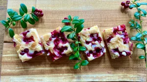 Slices of lingonberry and almond cake topped with fresh berries and almond slivers on a wooden board