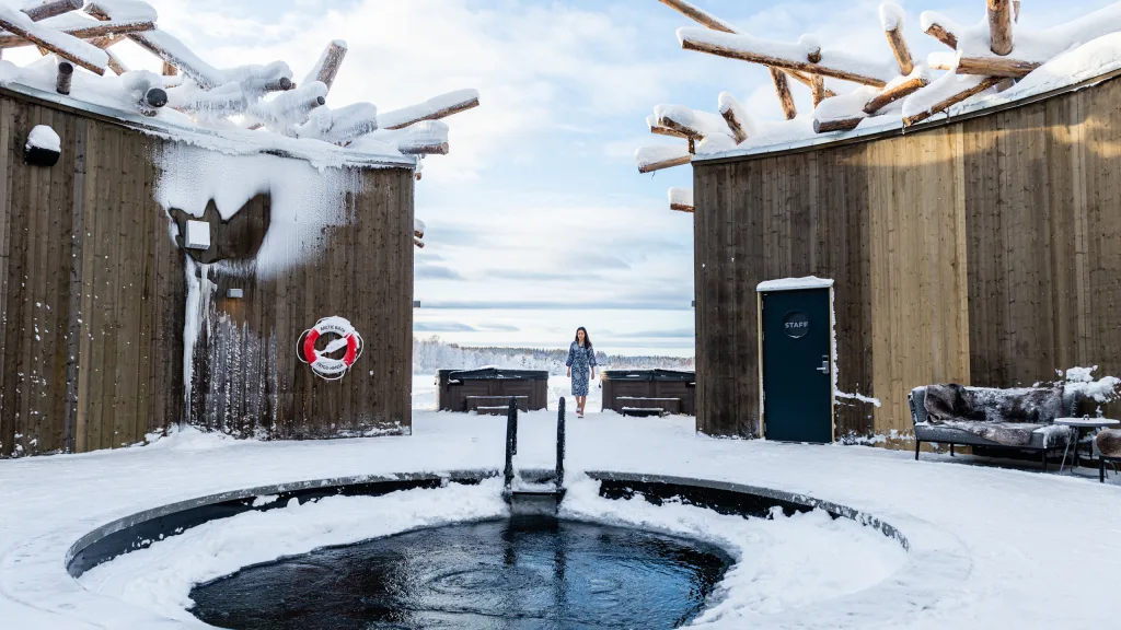 Guest in a robe walking toward a circular cold plunge pool in Arctic Bath's snowy courtyard