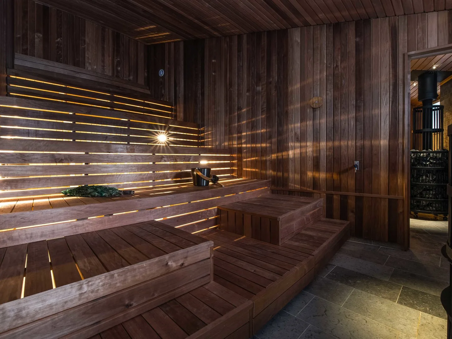 Warmly lit wooden sauna with tiered benches, birch whisk and stone stove at Arctic Bath