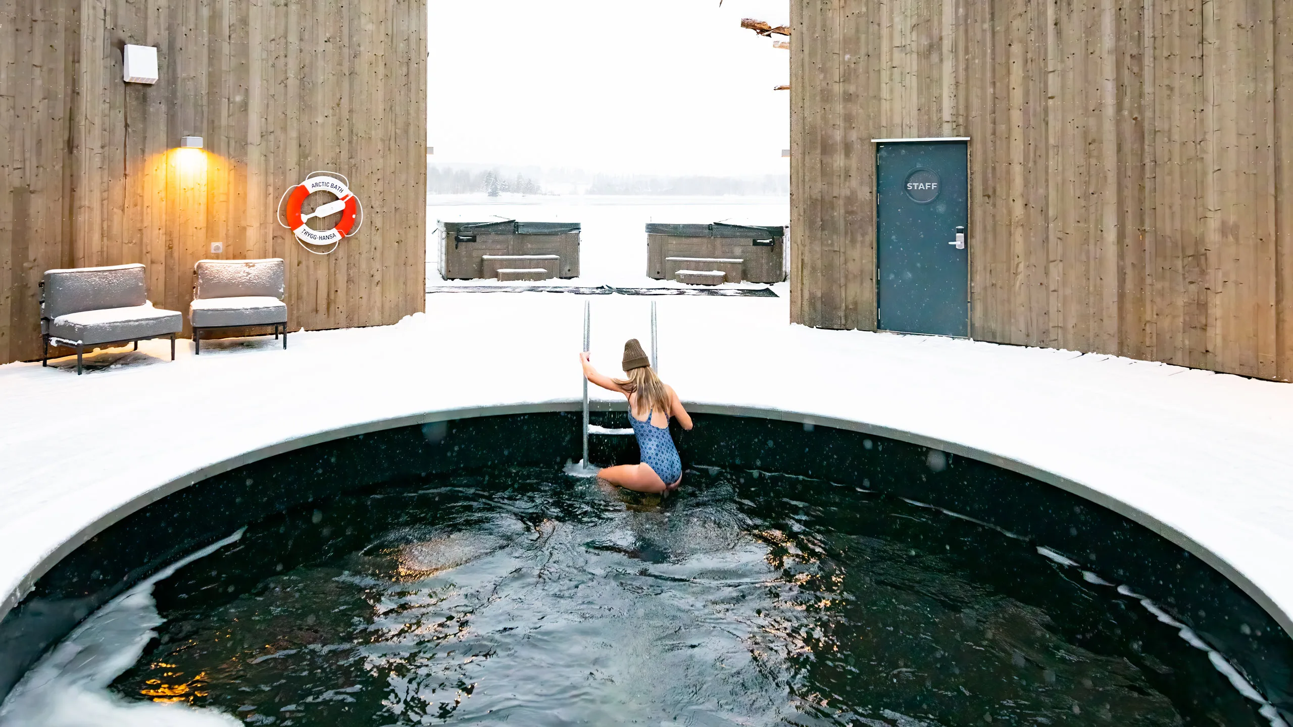 Guest stepping into a circular ice bath surrounded by curved wooden walls at the Arctic Bath spa in winter