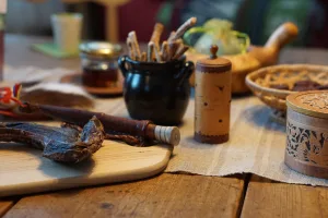 Rustic table spread with dried reindeer meat, birch-bark containers, breadsticks, and a traditional Sámi knife