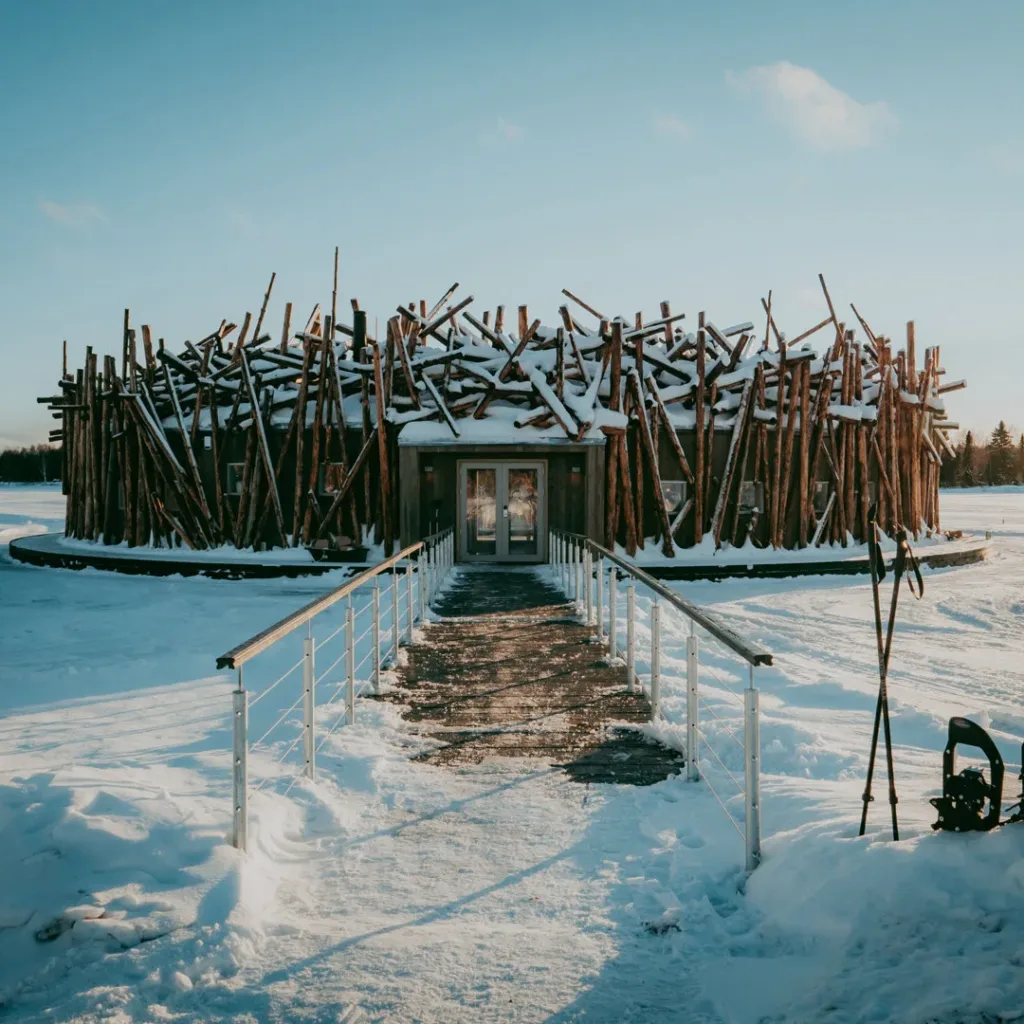 Arctic Bath main building in winter sunlight with snowshoes and trekking poles planted in the snow in the foreground